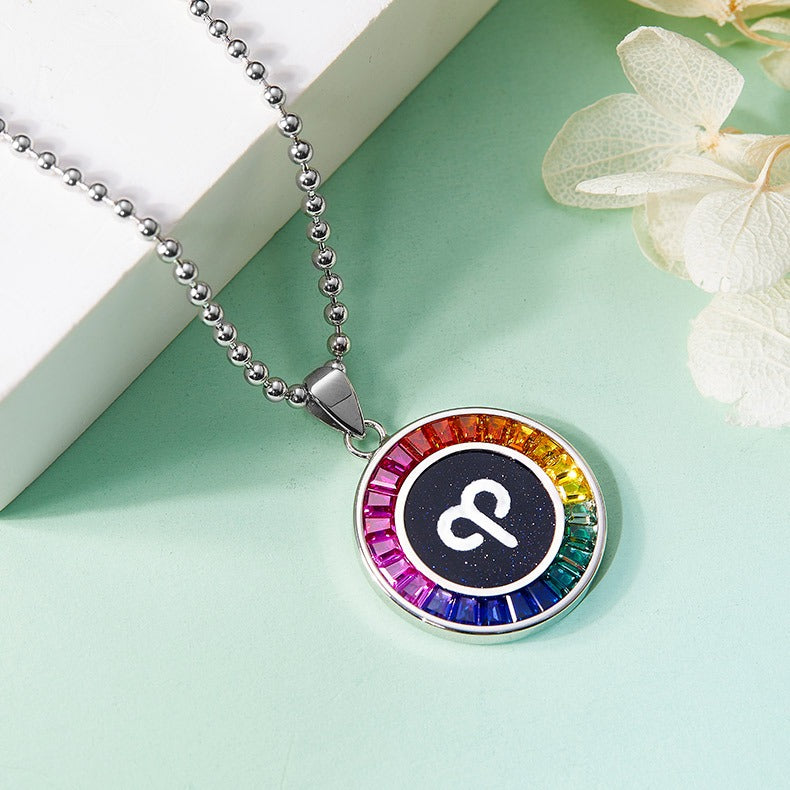 Necklace with a colorful pendant featuring a Aries symbol on a light green surface with flowers.