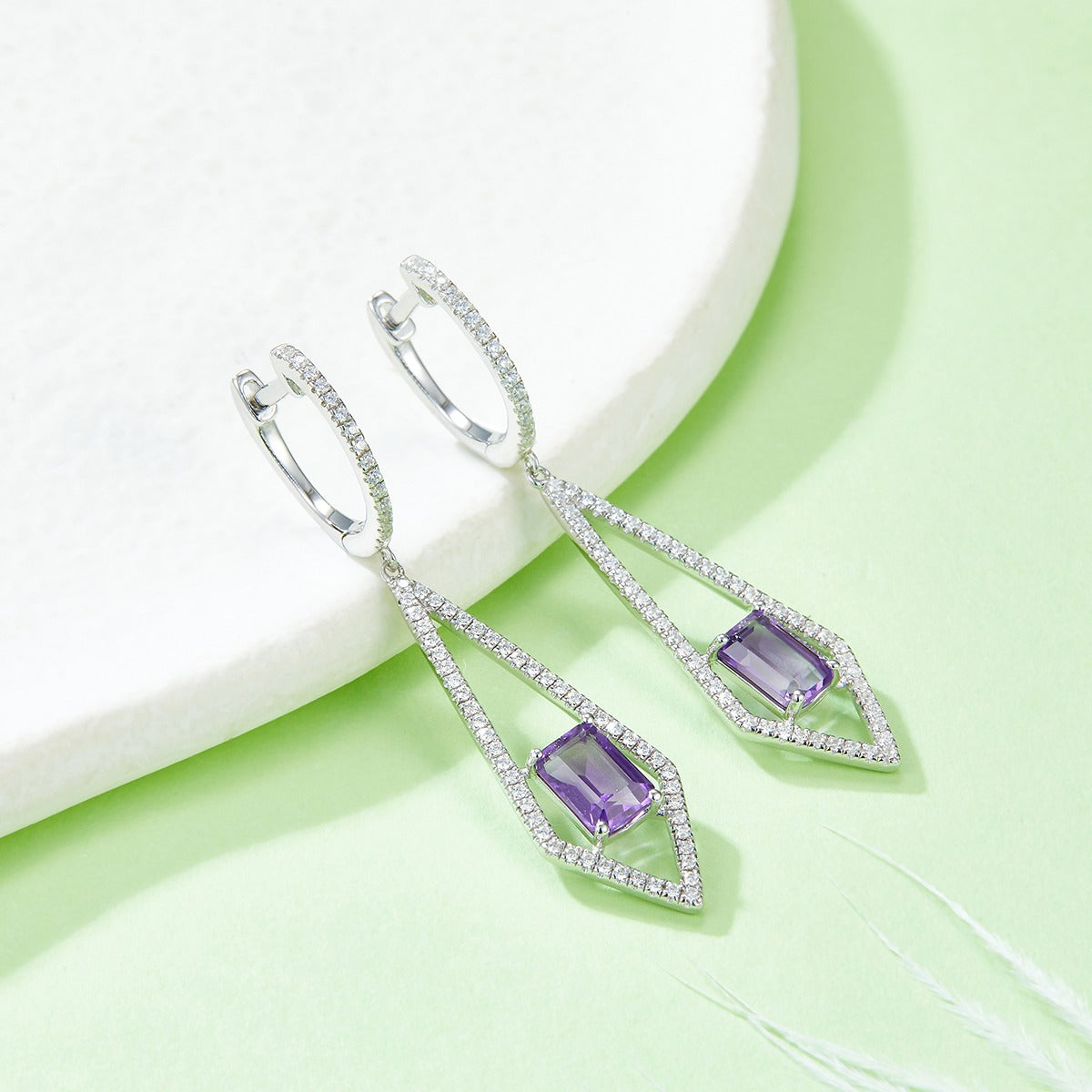 Silver earrings with purple amethyst gemstones on a light green background