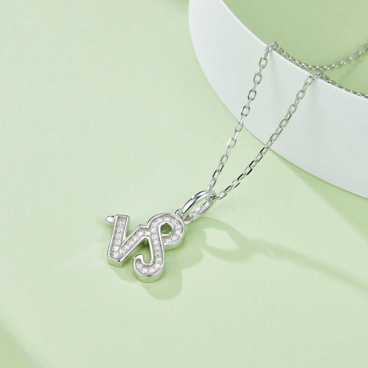 Silver necklace with a 'WJ' pendant on a light green background