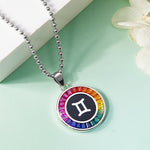 Necklace with a Gemini zodiac sign pendant featuring a rainbow-colored border on a light green background.