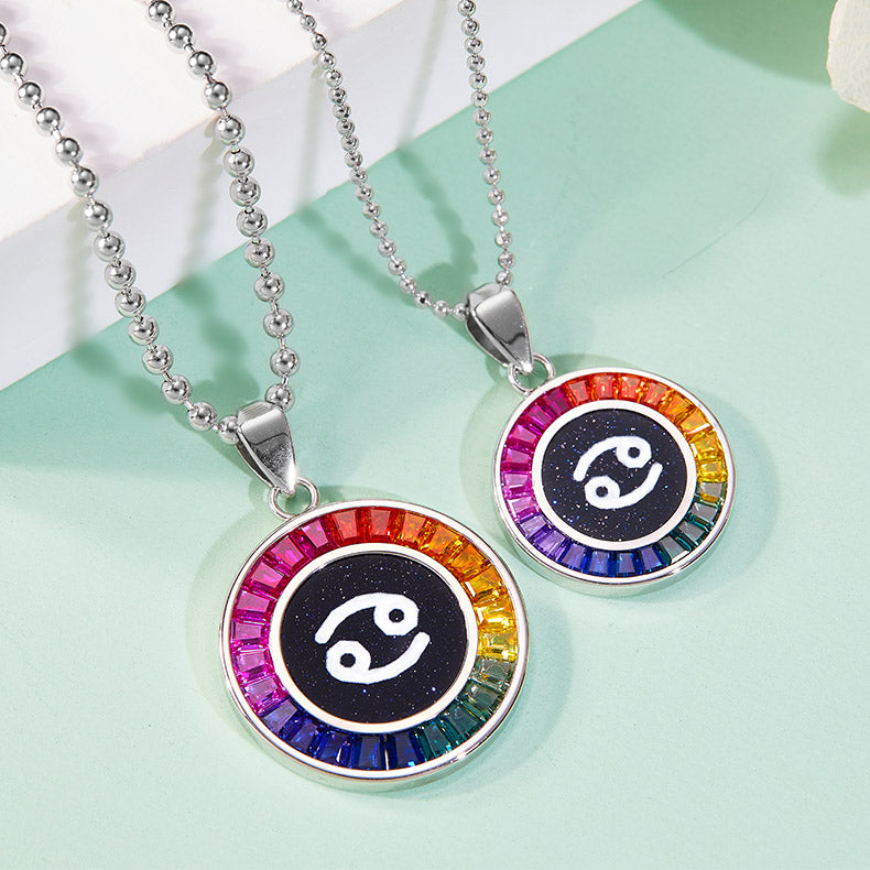 Two zodiac-themed necklaces with rainbow accents on a light green background