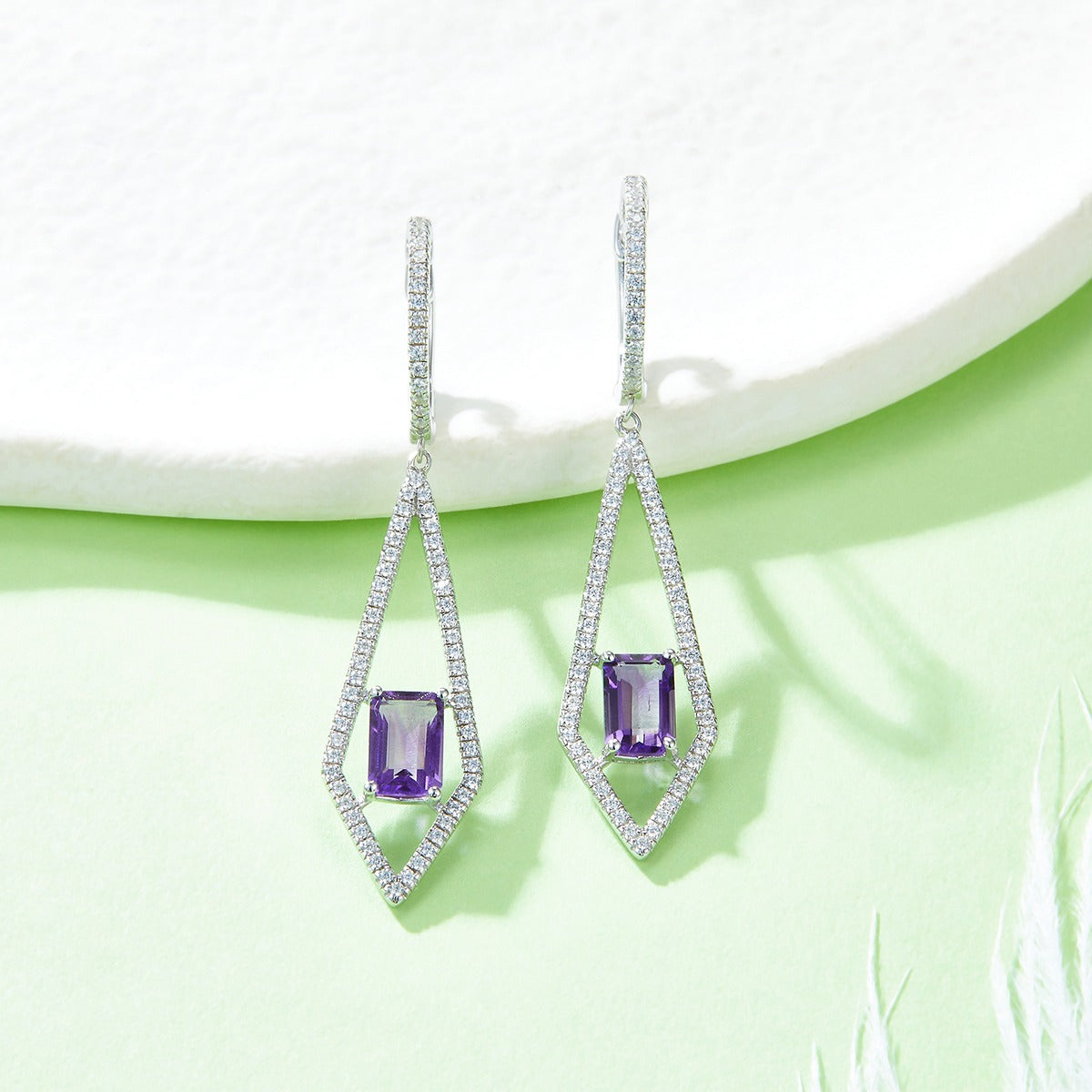 Pair of earrings with purple amethyst  gemstones on a light green background