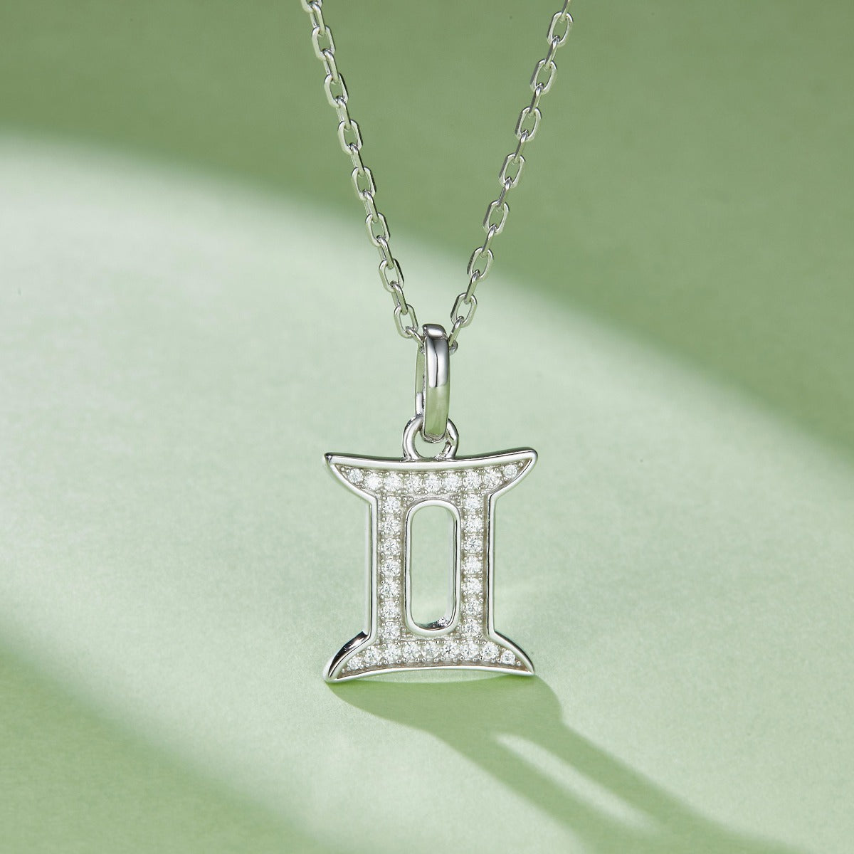 Silver Gemini zodiac pendant necklace on a light green background
