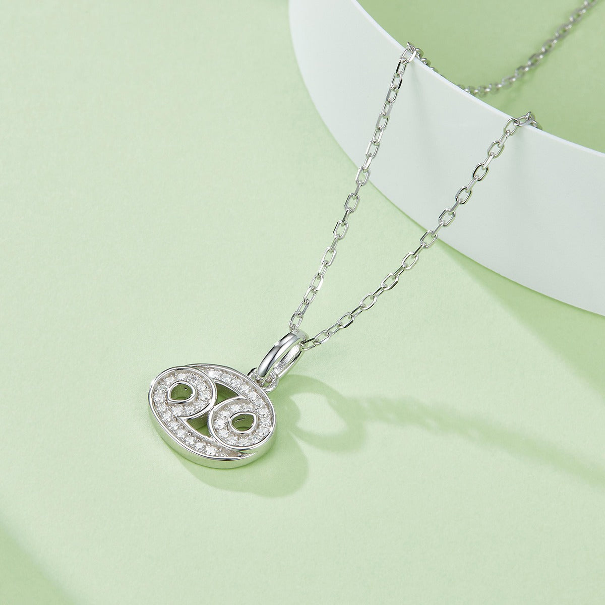 Silver necklace with a heart-shaped pendant on a light green background