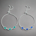 Two silver bracelets with green and blue gemstones on a gray background
