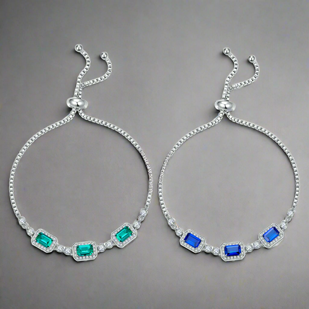 Two silver bracelets with green and blue gemstones on a gray background