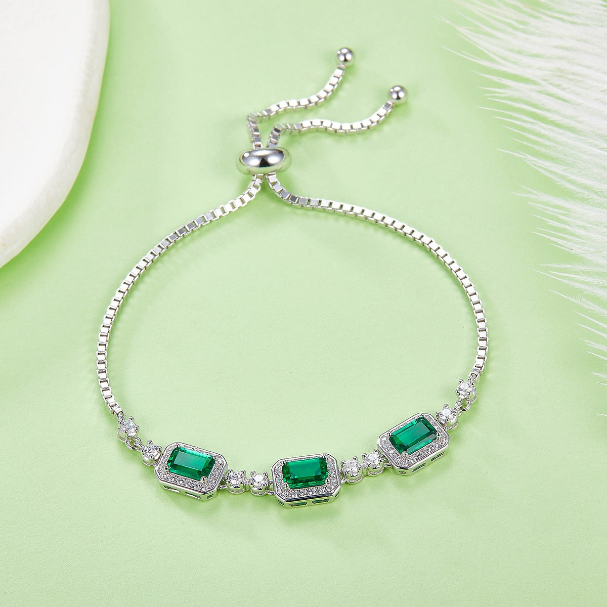 Silver bracelet with green emerald  gemstones on a light green background