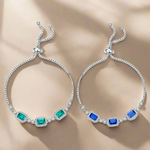 Two silver bracelets with green and blue gemstones on a yellow background