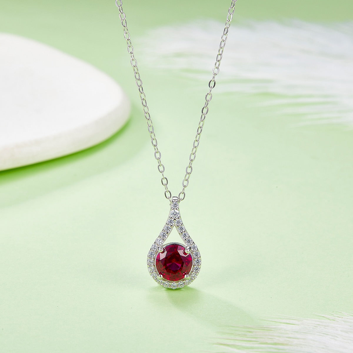 Silver necklace with a red gemstone pendant on a light green background