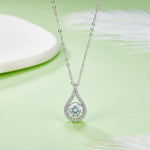 Teardrop-shaped diamond pendant on a chain against a light green background