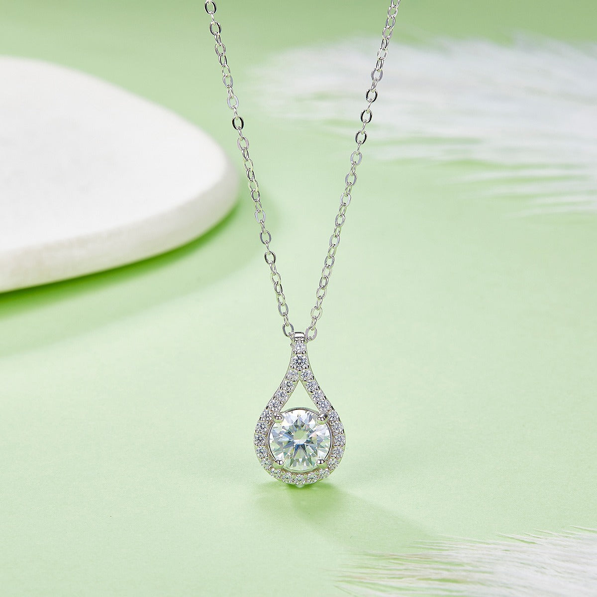 Teardrop-shaped diamond pendant on a chain against a light green background
