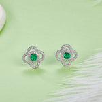 Pair of silver earrings with green emerald gemstones on a light green background