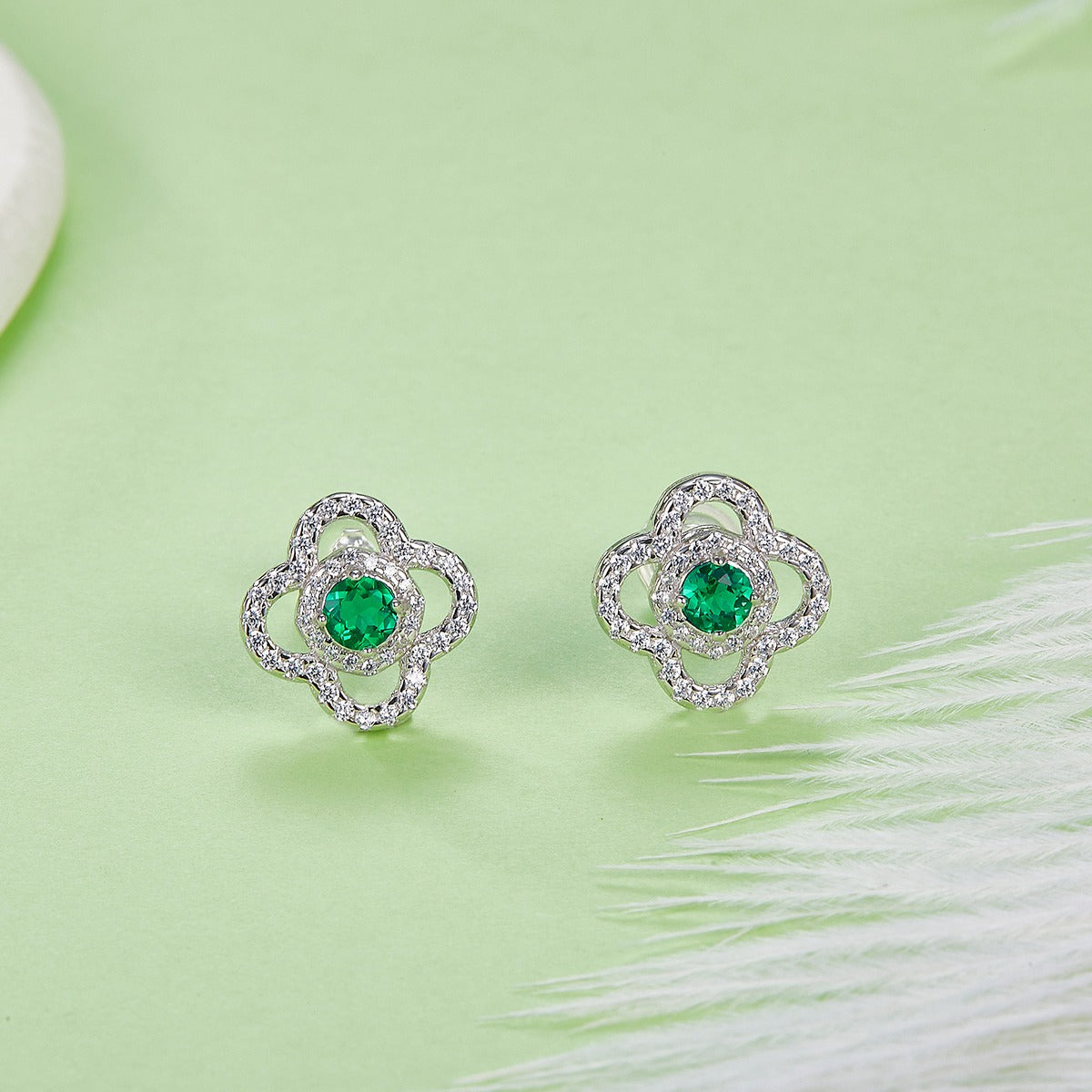 Pair of silver earrings with green emerald gemstones on a light green background