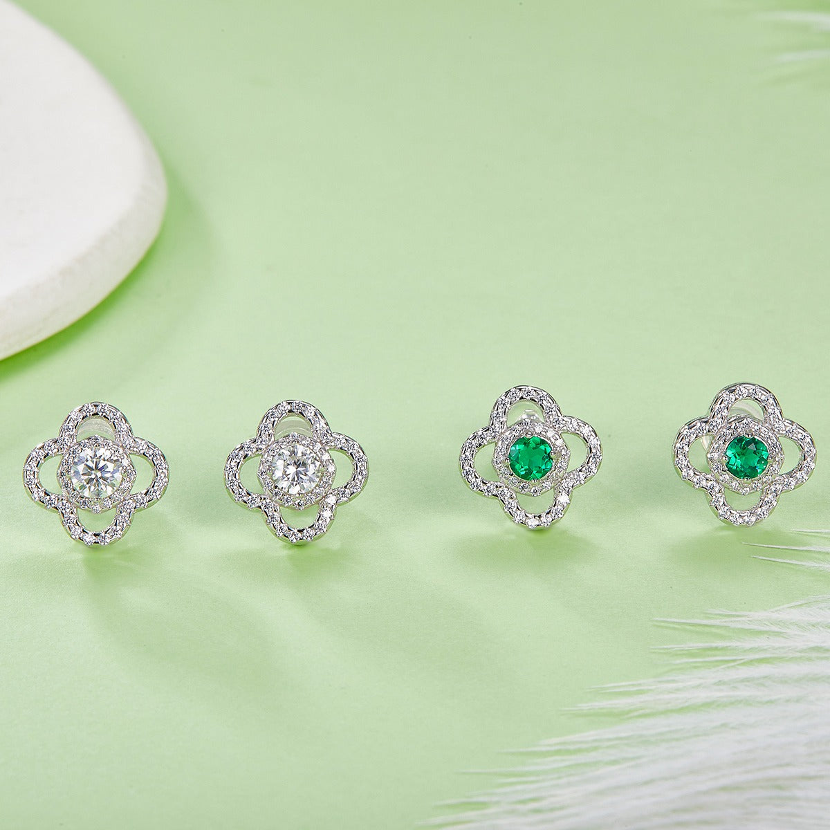 Four pairs of earrings with green emerald gemstones on a light green background