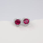 Heart-shaped earrings with red gemstones on a light gray background