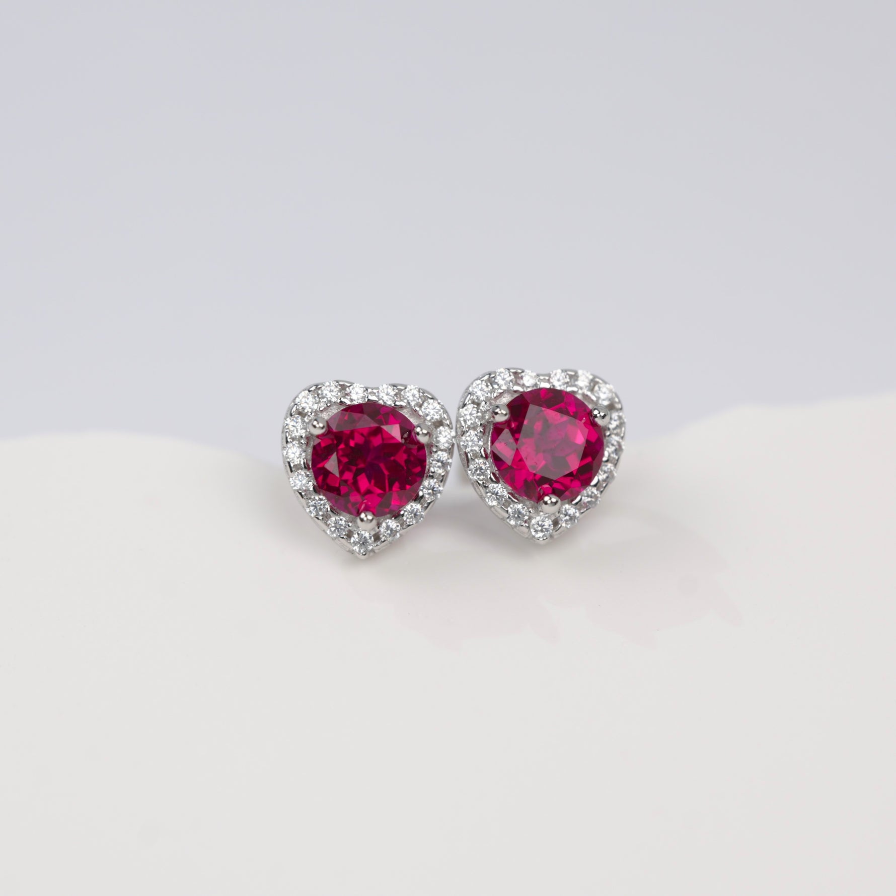 Heart-shaped earrings with red gemstones on a light gray background